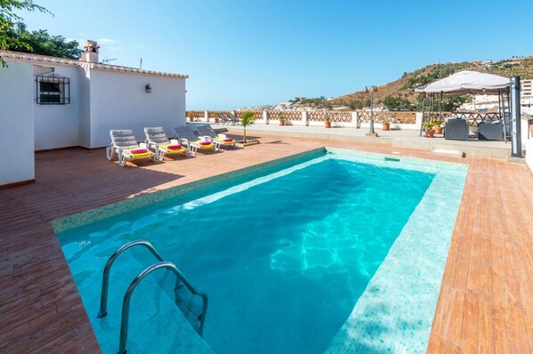Una piscina rectangular con muelle de madera y sillones de descanso.
