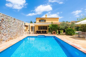 A swimming pool with a stone wall, a yellow building with a tiled roof, and outdoor furniture. - Villa 'Can Magraner' with Mountain View, Wi-Fi and Air Conditioning (Port de Pollensa)