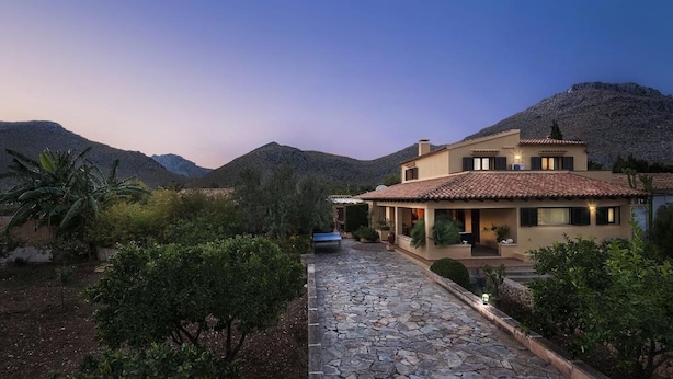 A two-story house with a stone pathway leading to the entrance, surrounded by greenery and mountains in the background. - Villa 'Can Magraner' with Mountain View, Wi-Fi and Air Conditioning (Port de Pollensa)