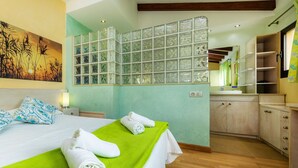 A hotel room with a bed, a green towel, a bathroom with a mirror, and a view of the outside. - Villa 'Can Magraner' with Mountain View, Wi-Fi and Air Conditioning (Port de Pollensa)