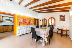 A kitchen with wooden beams, a dining table with chairs, and a large painting on the wall. - Villa 'Can Magraner' with Mountain View, Wi-Fi and Air Conditioning (Port de Pollensa)
