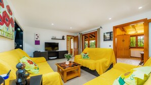 A living room with yellow sofas, a wooden coffee table, a TV, and a door leading to an outdoor area. - Villa 'Can Magraner' with Mountain View, Wi-Fi and Air Conditioning (Port de Pollensa)