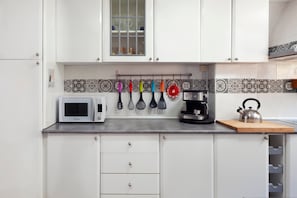 Uma cozinha com armários brancos, micro-ondas, chaleira e diversos utensílios pendurados na parede.