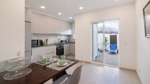 A modern kitchen with white cabinets, a dining table with chairs, and a glass door leading to a balcony.
