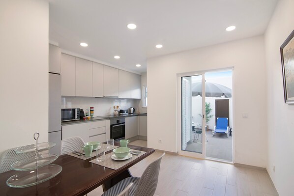 A modern kitchen with white cabinets, a dining table with chairs, and a glass door leading to a balcony.