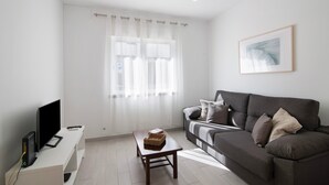 A modern living room with a flat-screen TV, a sofa, a coffee table, and a window with sheer curtains.