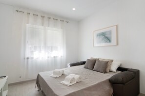 A bedroom with a bed, pillows, a framed picture, and a window with curtains.