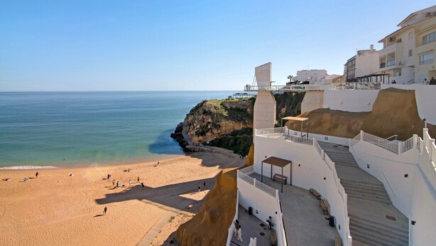 A coastal hotel with a beach view, a staircase leading to a terrace, and a clear sky.