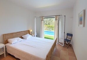 A bedroom with a bed, a nightstand, a chair, and a view of a swimming pool.