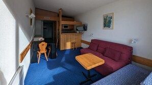 A compact room with a kitchenette, a red sofa, a wooden table, and a blue polka dot carpet.