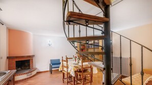 Eine Wendeltreppe, ein Kamin, ein Esstisch mit Stühlen und ein blauer Sessel in einem Raum mit Fliesenboden.