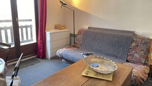 Een knus ogende kamer met een bank, een houten salontafel, een lamp en een raam met gordijnen.