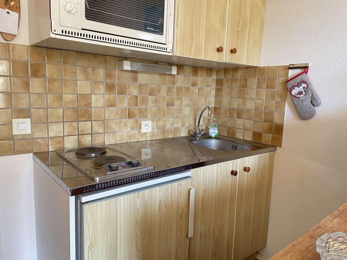 Een kleine keuken met een magnetron, fornuis en spoelbak.