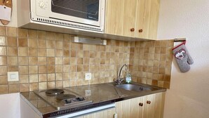 Een kleine keuken met een magnetron, fornuis en spoelbak.