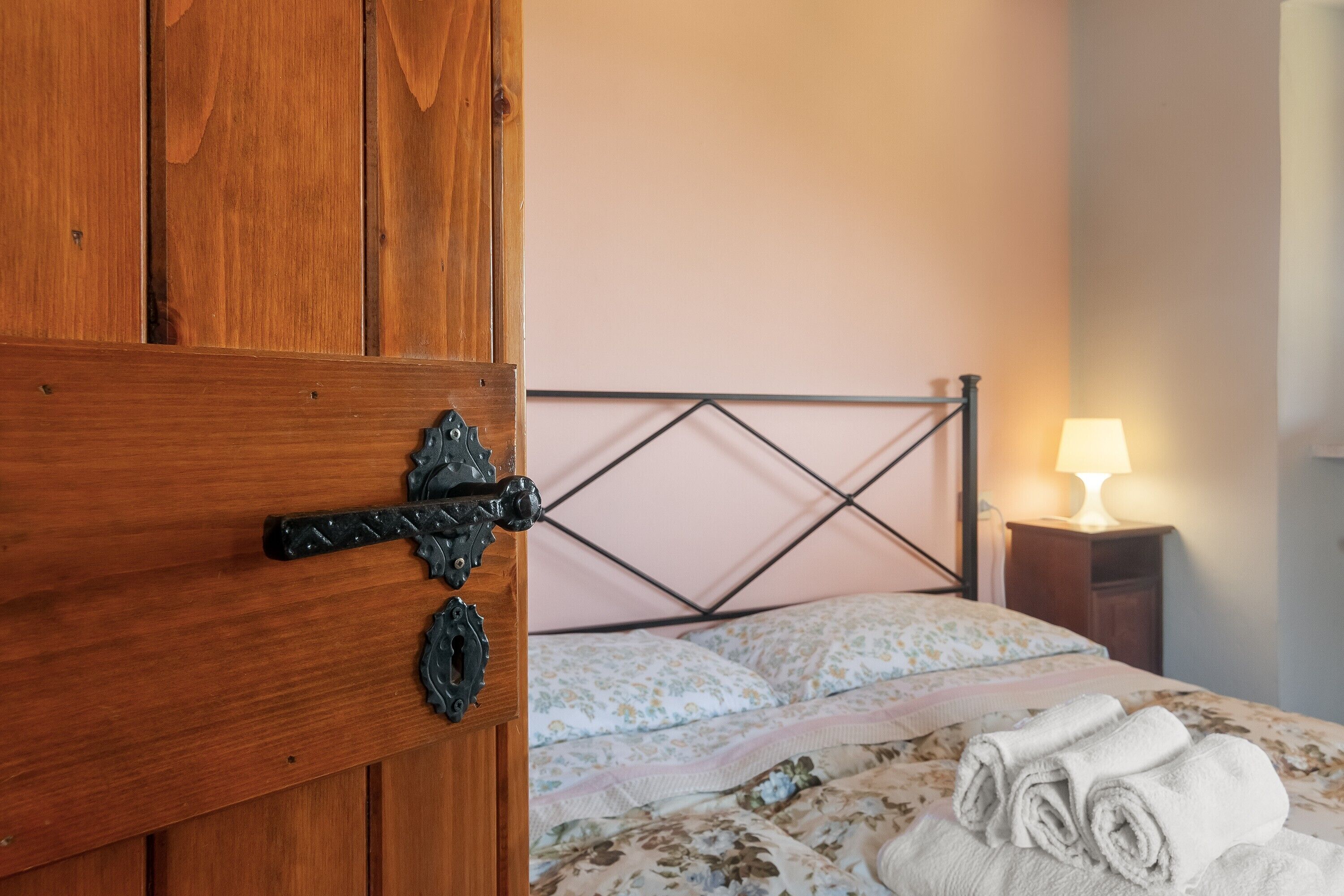Una puerta de madera con manija metálica, una cama con ropa de cama floral y una lámpara de noche.