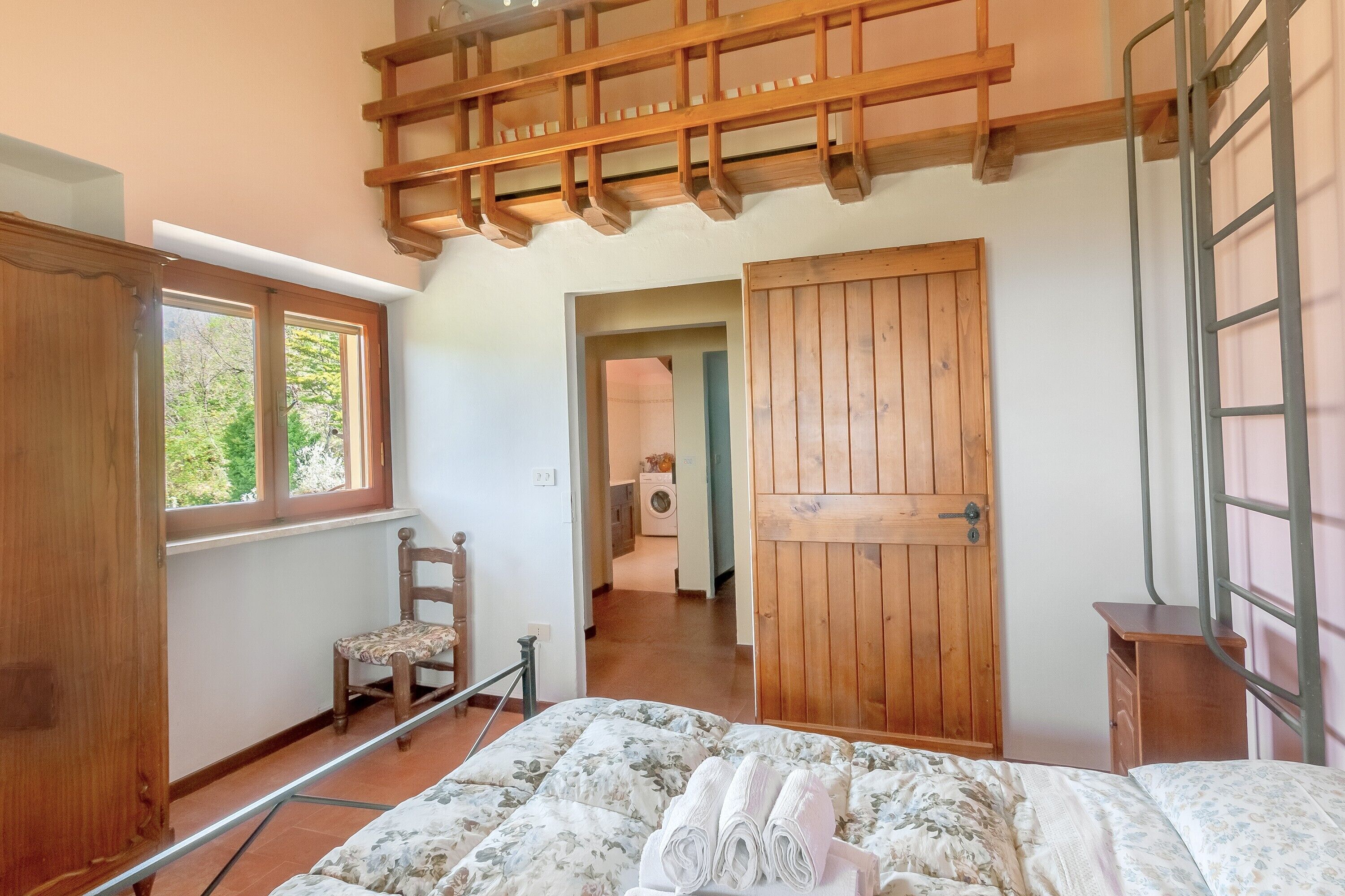 A bedroom with a bed, wooden wardrobe, a chair, a wooden door, and a window.