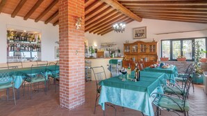A restaurant with brick pillars, wooden beams, and a bar area. Tables are set with green tablecloths and metal chairs. - Apartment 'La Tavernetta' with Shared Pool, Private Terrace and Wi-Fi (Castelfranco Piandiscò)