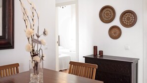 En matplats med ett träbord, stolar, en vas med torkade blommor och dekorativa tallrikar på väggen.