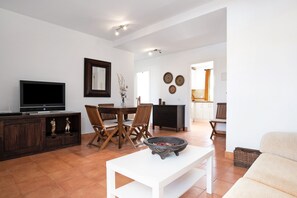 A living room with a TV, dining table, chairs, a white coffee table, and a fireplace.
