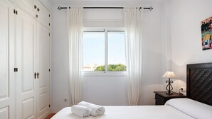 Ett hotellrum med en säng, ett fönster med gardiner, ett nattduksbord med en lampa och en garderob.