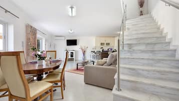 A modern living room with a dining area, a staircase, and a kitchen in the background.