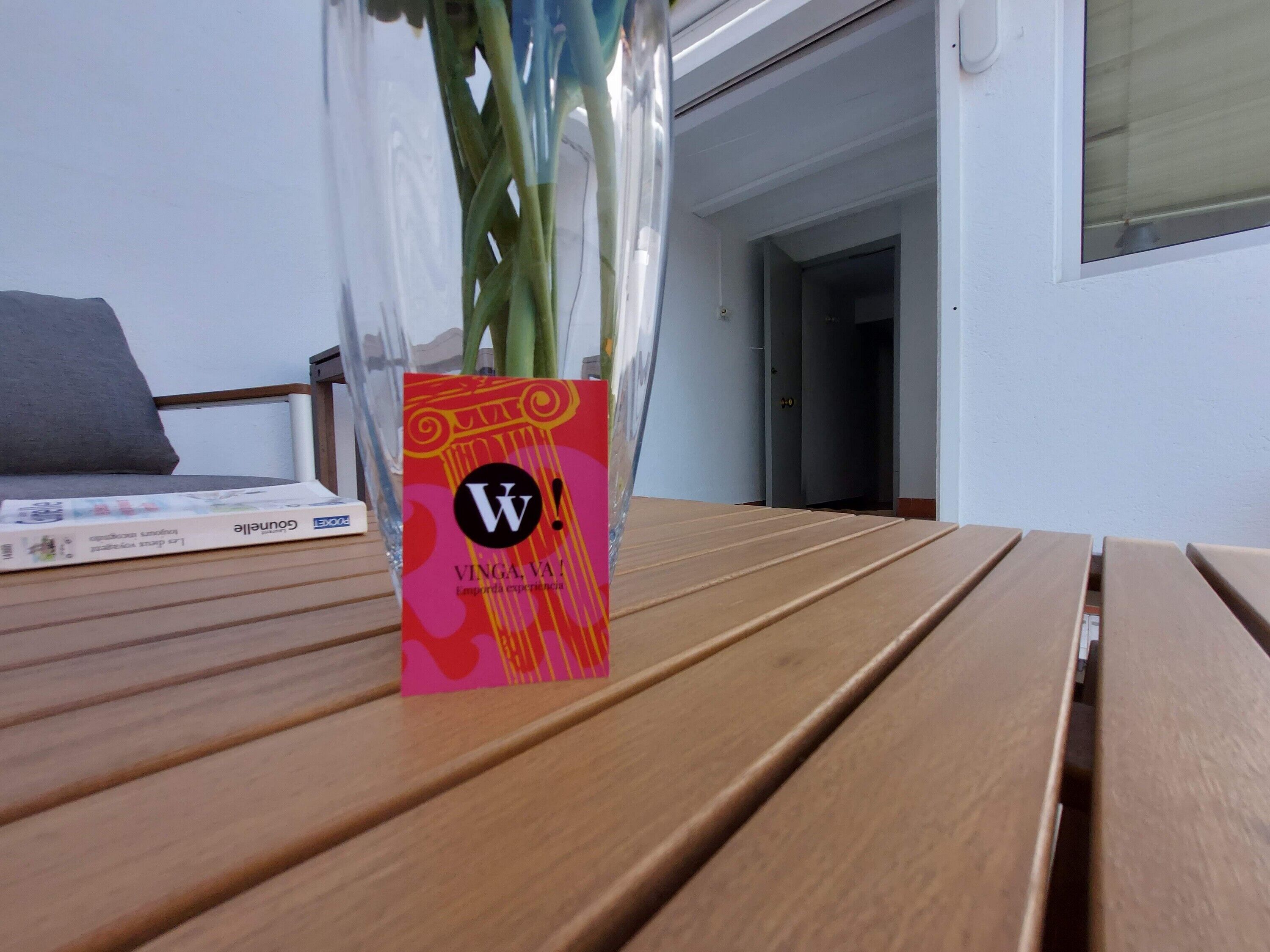 A wooden table with a vase of flowers and a colorful card.