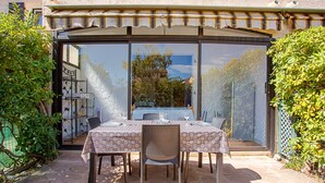 An outdoor patio with a table set for two, surrounded by chairs, and a glass door leading to a garden. - "Les Tulipes" Apartment with Private Terrace, Garden, and Wi-Fi (Carqueiranne)