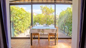 A dining area with a table and chairs, large windows, and a view of greenery. - "Les Tulipes" Apartment with Private Terrace, Garden, and Wi-Fi (Carqueiranne)