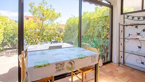 A room with a large window, a table with a tablecloth, and a metal shelf unit. - "Les Tulipes" Apartment with Private Terrace, Garden, and Wi-Fi (Carqueiranne)