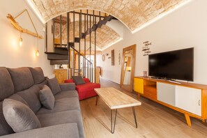 A modern living room with a grey sofa, red armchair, wooden TV stand, and a spiral staircase.