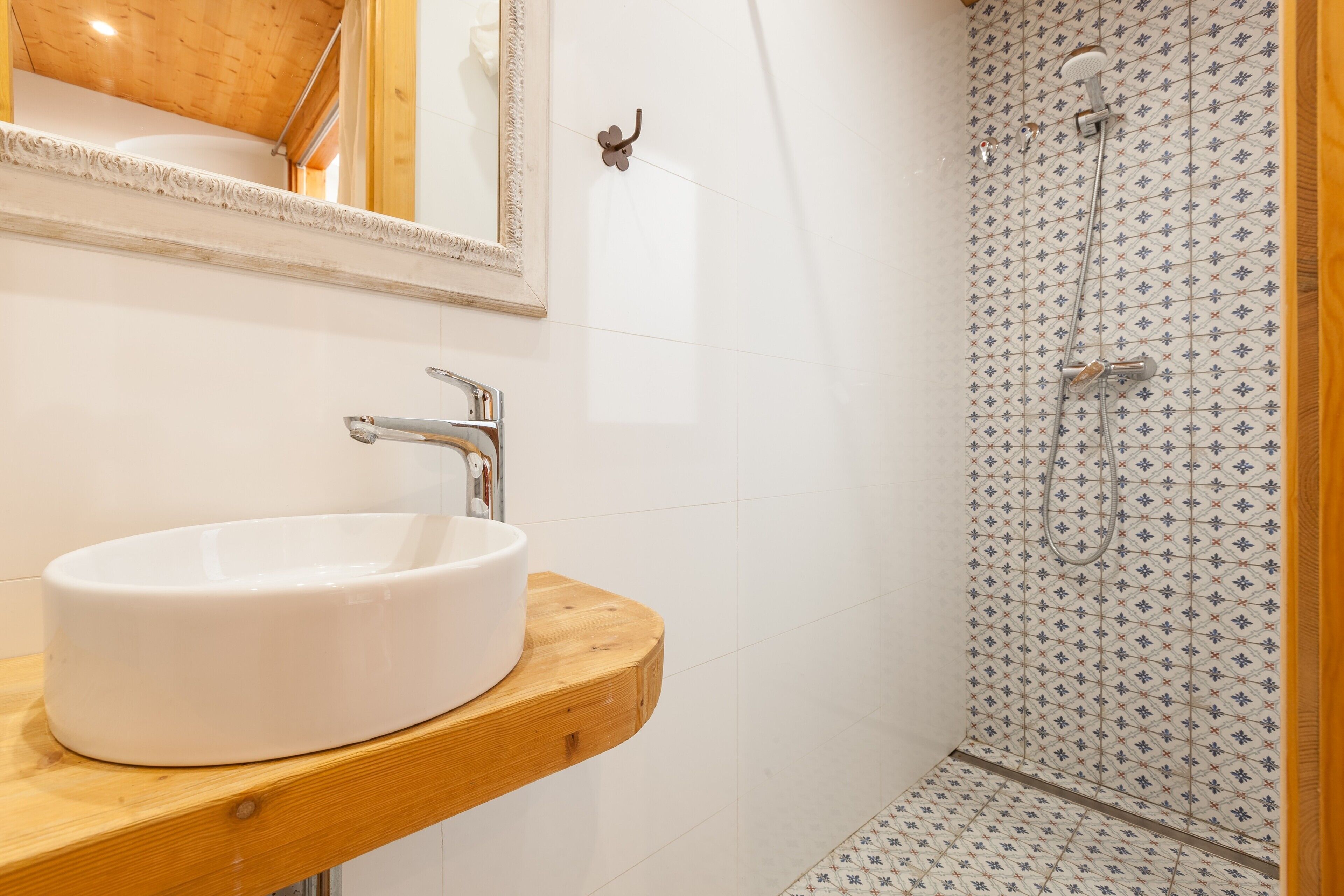 A bathroom with a white sink, wooden countertop, and a shower with patterned tiles.