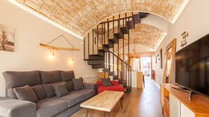 A modern living room with a curved staircase, a sofa, a coffee table, and a TV. - Sant Rafel House – Private Terrace, 5-Minute Walk to the Beach (ARENYS DE MAR)