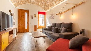 A living room with a sofa, a TV, a wooden table, and a ceiling with exposed beams. - Sant Rafel House – Private Terrace, 5-Minute Walk to the Beach (ARENYS DE MAR)