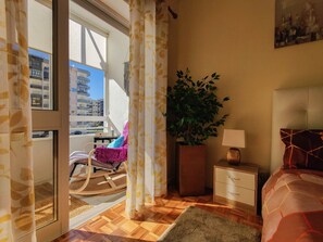 A bedroom with a view of buildings, a potted plant, a wooden floor, a bed, a nightstand, and a chair. - Apartment 'Bosque Marítimo' with Mountain View, Private Terrace and Wi-Fi (Chafé)