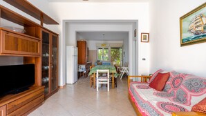 A living room with a TV, wooden cabinets, a dining area with a table and chairs, and a sofa with patterned cushions. - Villa "Tina" Close to the Beach and the City (torre lapillo)