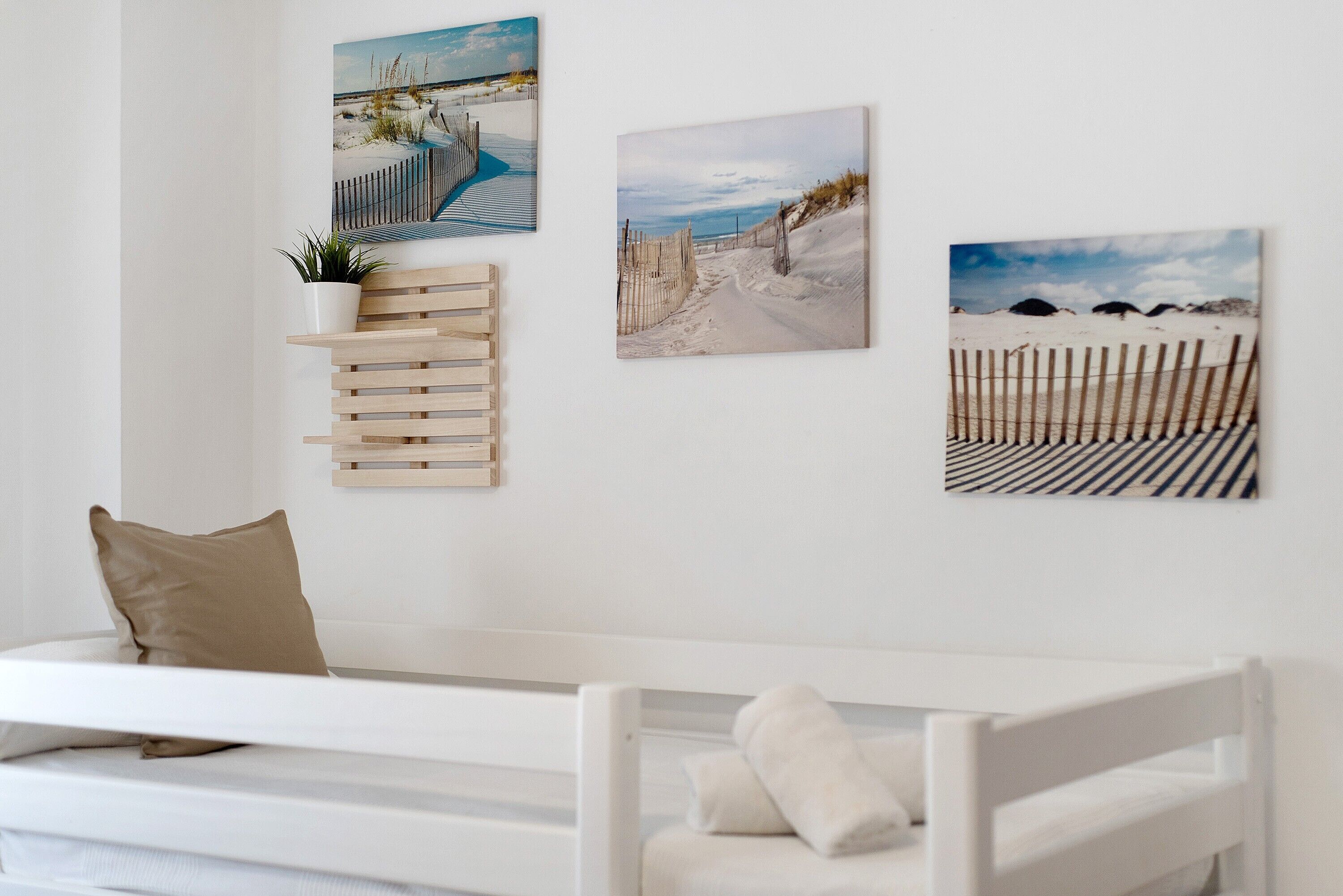 Una culla bianca con un cuscino beige, uno scaffale in legno con una pianta e tre elementi decorativi a tema spiaggia.