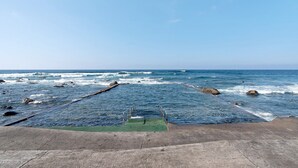 A concrete staircase leading to a rocky shoreline with waves crashing onto the rocks.