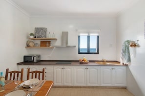 A compact kitchen with white cabinetry, a microwave, a sink, and a window with a view. - Vacation Home "El Altillo House" with Sea View, Shared Terrace & Wi-Fi (Moya)