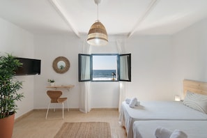 A bedroom with a bed, a desk, a chair, a TV, a window with curtains, and a view of the sea. - Vacation Home "El Altillo House" with Sea View, Shared Terrace & Wi-Fi (Moya)