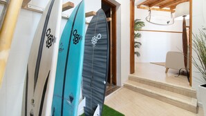 A hallway with surfboards leaning against the wall, a staircase, and a room with a chair and a lamp.