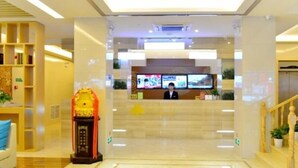 Un vestíbulo de hotel con una recepción, un reloj grande y una escalera que conduce a los pisos superiores.