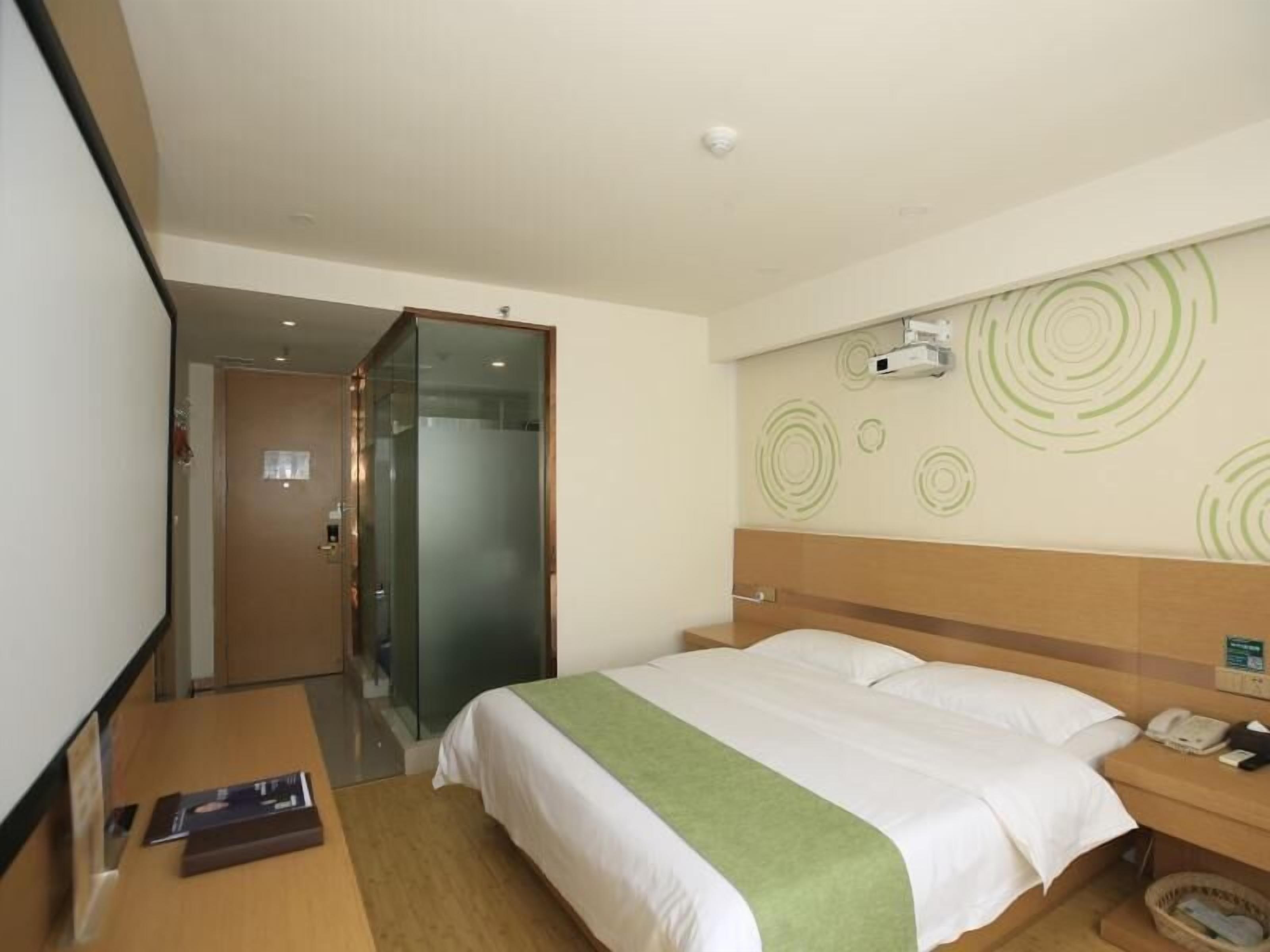 A hotel room with a bed, bedside table, and a wall-mounted projector.