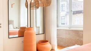 Une chambre d’hôtel moderne, dotée d’un grand miroir, de deux vases en terre cuite et offrant une vue sur la ville par une fenêtre.