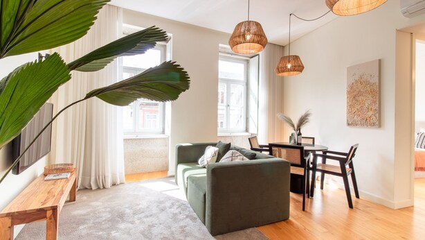 Un salon moderne avec un canapé vert, une table basse en bois et des suspensions en osier.