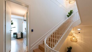 Un escalier moderne avec une rampe blanche, un plancher en bois et un luminaire fixé au mur.