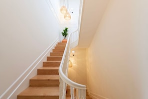 A staircase with wooden steps and white railings, leading to a landing with a plant and a wall-mounted light fixture.
