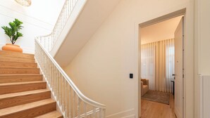 Una escalera de madera con balaustres blancos que conduce a una habitación con una puerta y una pequeña zona de estar.