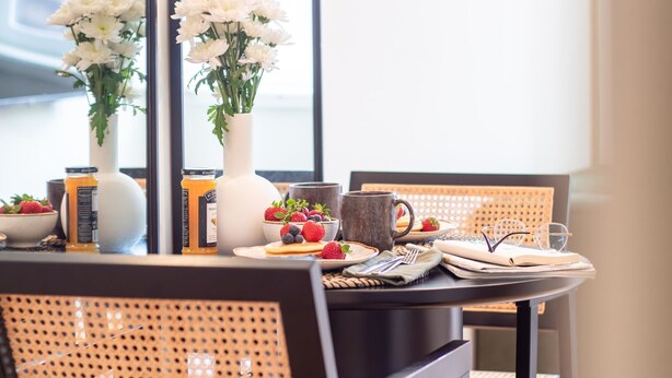 A dining table with a white vase, a bowl of strawberries, a jar of jam, and a mug. - Mouzinho 215 - Apartment 303 by LovelyStay (Porto)