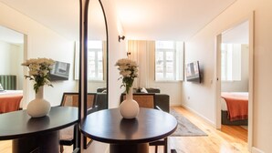 A modern living room with a round table, two white vases with flowers, a sofa, and a television. - Mouzinho 215 - Apartment 303 by LovelyStay (Porto)