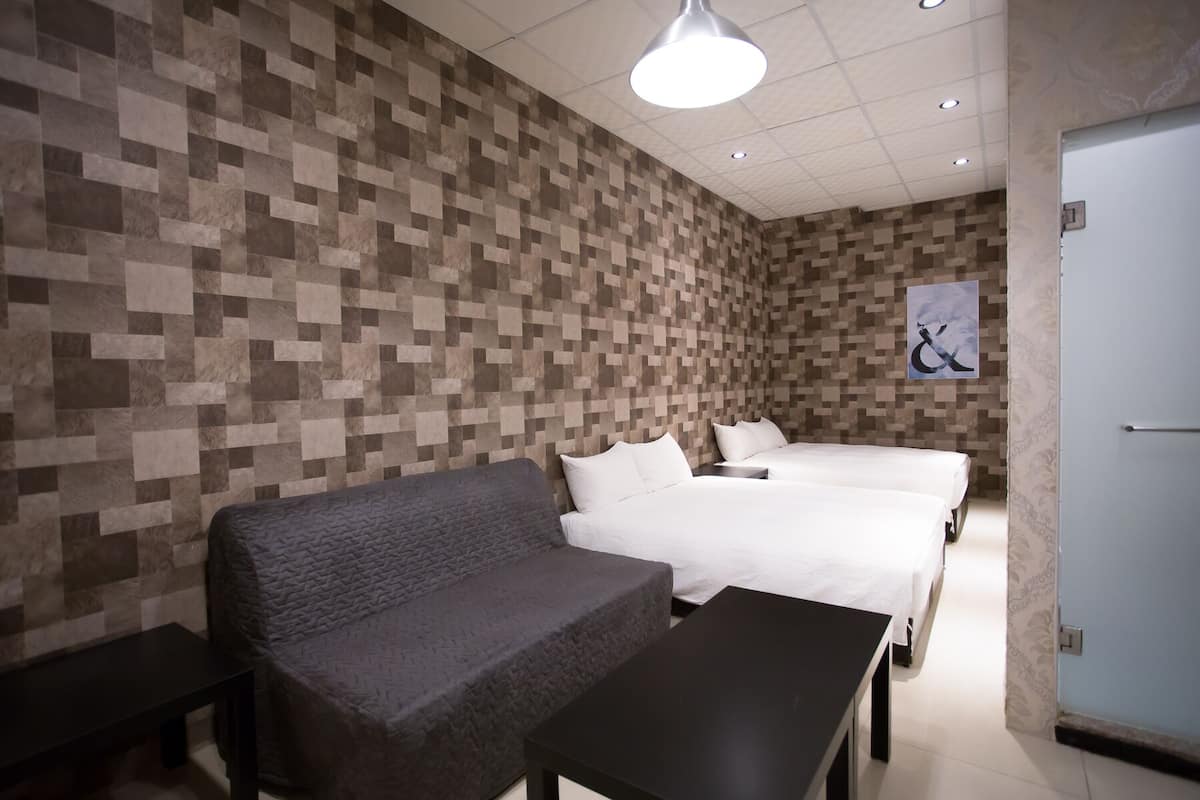 A hotel room with a modern design, featuring a textured wall, a sofa, two beds, and a small table.